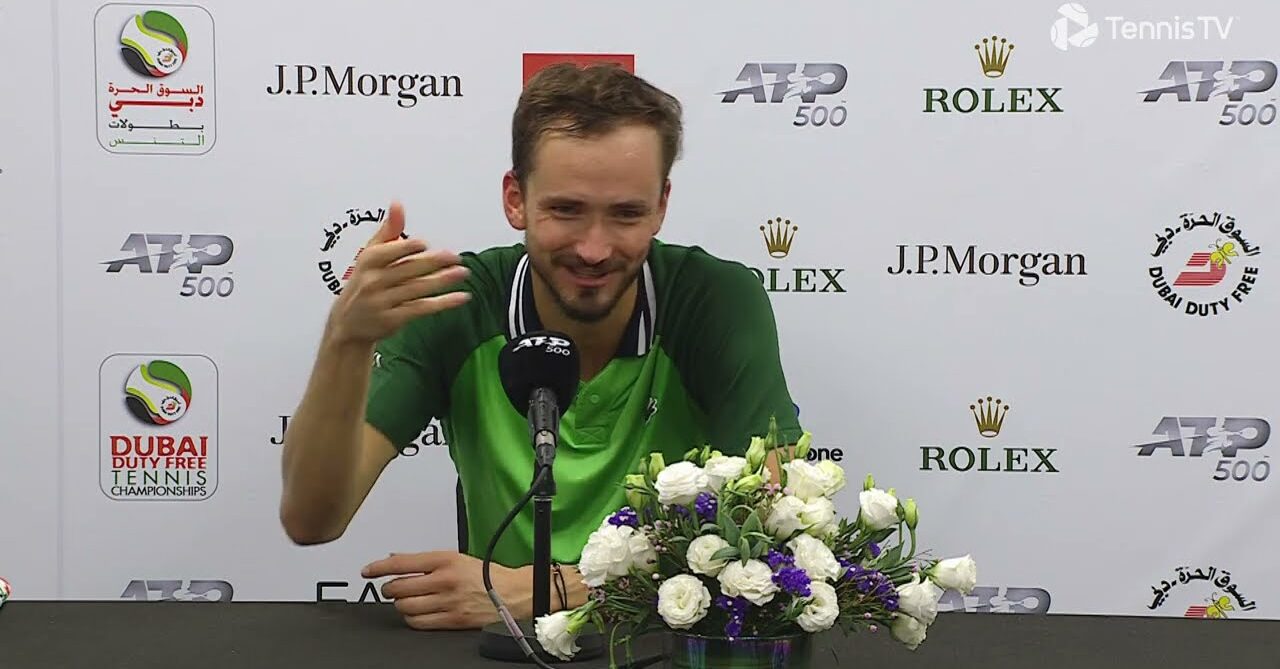 Daniil Medvedev behind the interview desk with a bouquet of flowers in front him and the Dubai tournament step-and-repeat