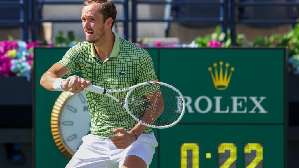 Daniil Medvedev, wearing a green patterned polo shirt and white shorts, plays tennis on a bright court, holding his racket mid-action. A green sign with the gold Rolex logo and a digital timer showing "0:22" are visible in the background.